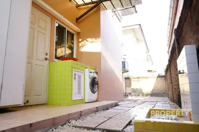 Charming outdoor laundry area with washing machine and tiled pathway in a cozy residential setting.