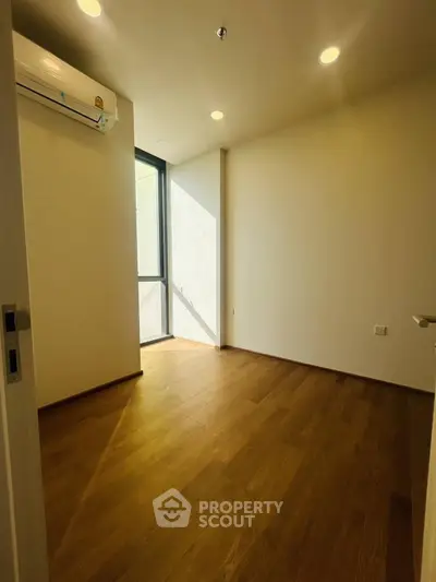 Bright empty room with wooden flooring and large window, perfect for customization.