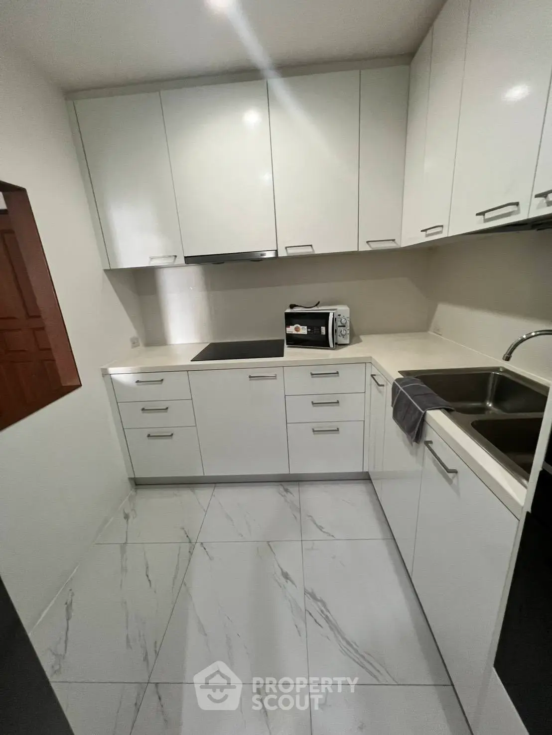 Modern white kitchen with sleek cabinets and marble floor tiles, featuring a built-in stove and microwave.