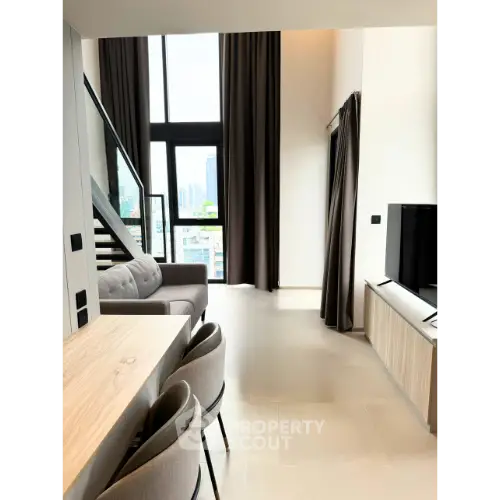 Modern living room with high ceiling and city view, featuring stylish furniture and large windows.
