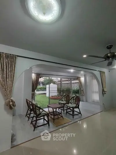 Spacious living room with elegant archway and garden view, featuring stylish wicker furniture.