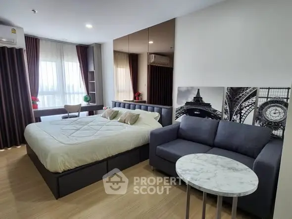 Modern studio apartment with cozy bed and stylish sofa, featuring large windows and elegant decor.