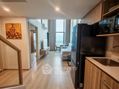 Modern open-plan living room with kitchen, featuring sleek appliances and large windows with scenic views.