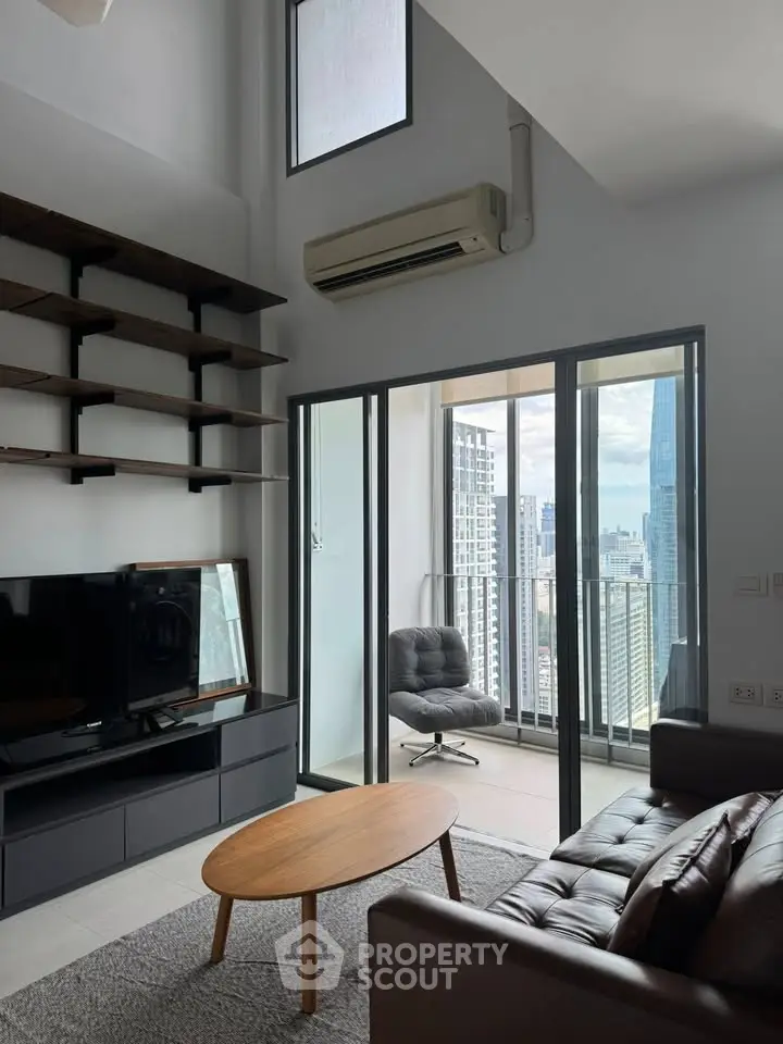 Modern living room with balcony and city view, featuring sleek furniture and high ceilings.