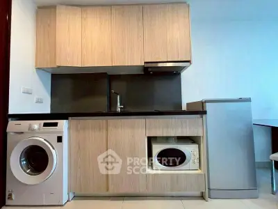 Modern kitchen with sleek cabinets, washing machine, and microwave in compact layout.