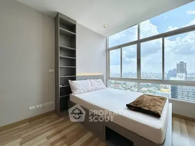 Modern bedroom with large windows offering stunning city views, featuring a cozy bed and built-in shelving.