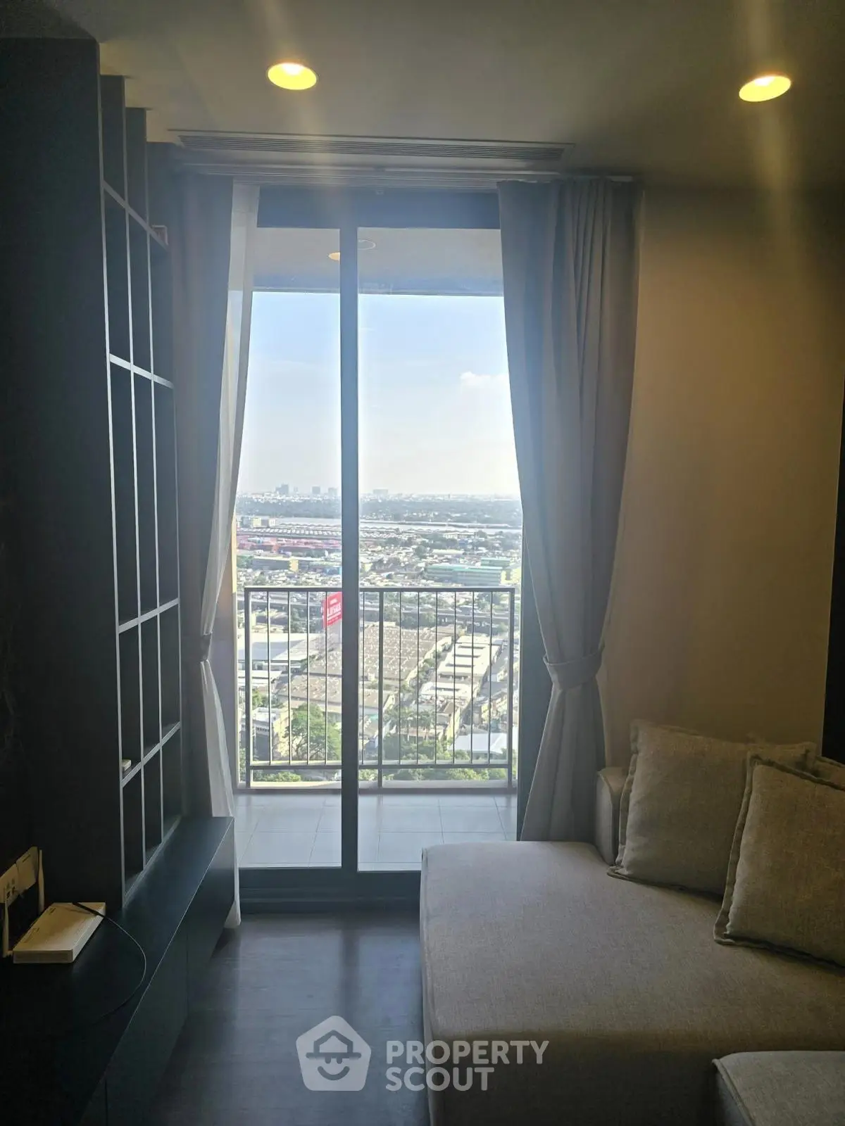 Modern living room with balcony offering stunning city view, featuring cozy sofa and elegant decor.