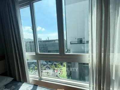 Bright window view from modern apartment overlooking cityscape and green area.