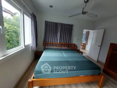 Spacious bedroom with large windows and modern ceiling fan in a serene setting.