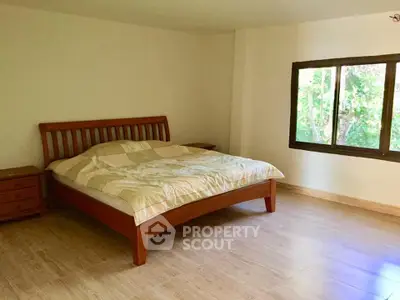 Spacious bedroom with wooden bed frame and large window overlooking greenery