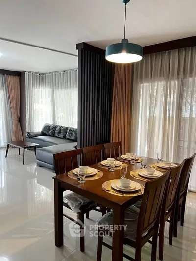 Elegant dining area with wooden table and chairs, adjacent to a cozy living room with a black leather sofa.
