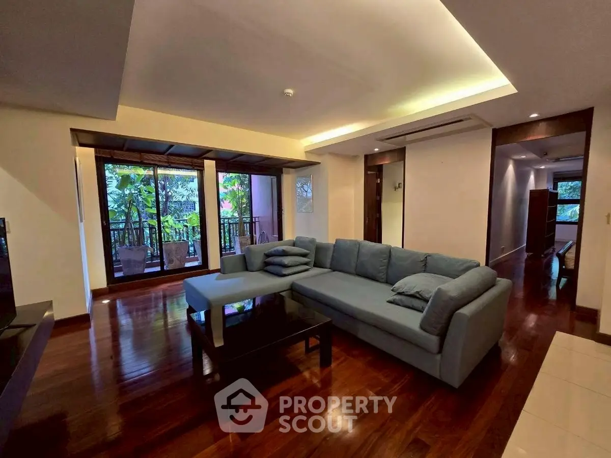 Spacious living room with elegant wooden flooring and large windows opening to a lush balcony view.
