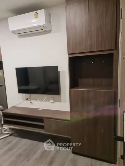Modern living room with sleek wooden cabinetry and mounted TV, featuring a minimalist design and air conditioning.