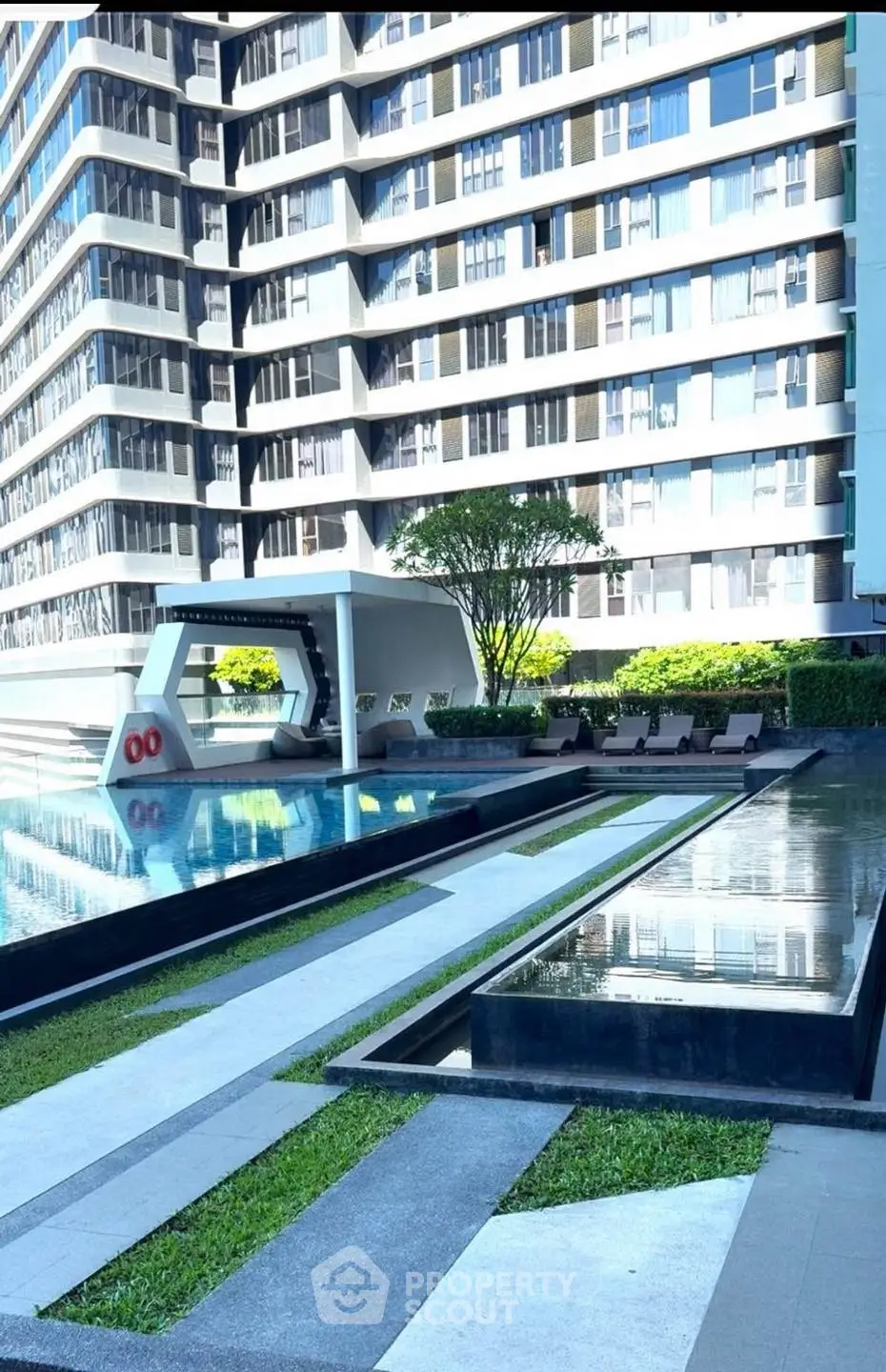 Luxurious modern apartment building with stunning poolside view and lush greenery.