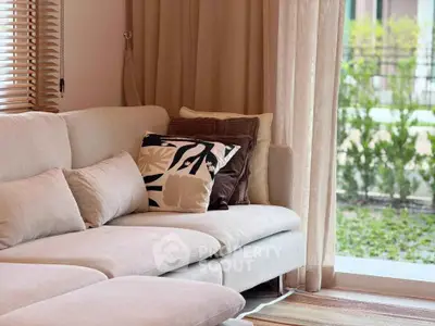 Cozy living room with plush beige sofa and stylish cushions, overlooking a lush garden through large windows.