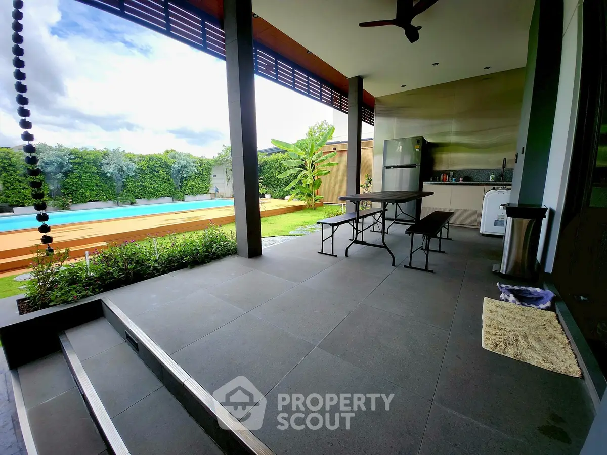 Luxurious poolside patio with modern outdoor kitchen and lush garden view.