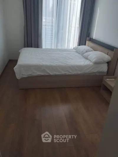 Modern bedroom with wooden flooring and large window for natural light.