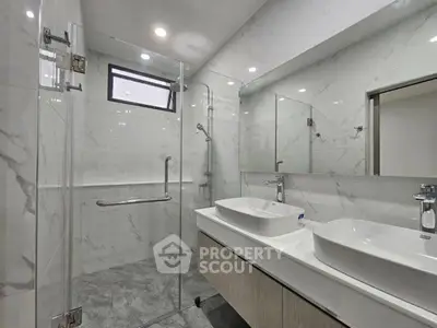 Modern bathroom with dual sinks and glass shower enclosure in sleek design.