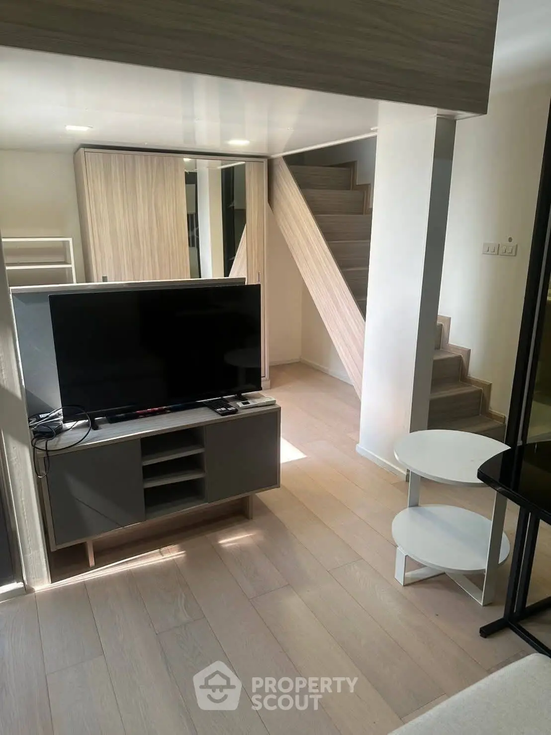 Modern living room with sleek TV setup and stylish staircase in a contemporary apartment.