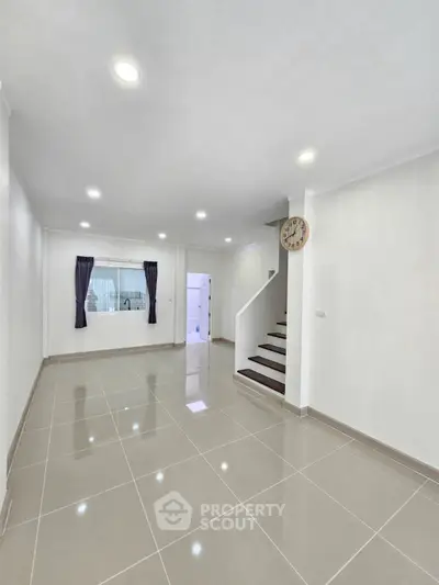 Spacious modern living room with glossy tiled floors and staircase, ideal for family gatherings.