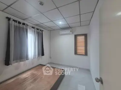 Minimalist bedroom with bed frame, air conditioning, and natural light through windows.