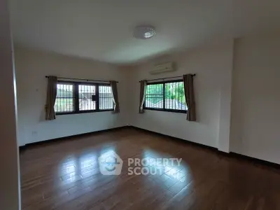Spacious empty room with wooden flooring and large windows, perfect for customization.