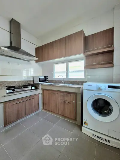 Modern kitchen with washing machine and wooden cabinets, featuring a gas stove and microwave.