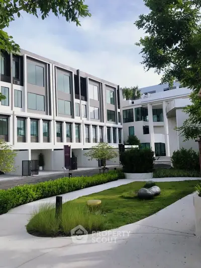 Modern building exterior with lush garden and sleek architectural design.