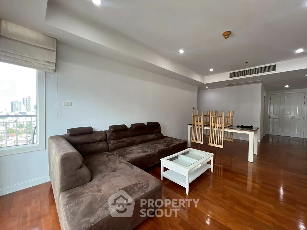 Spacious living room with modern brown sectional sofa and dining area, featuring wooden flooring.