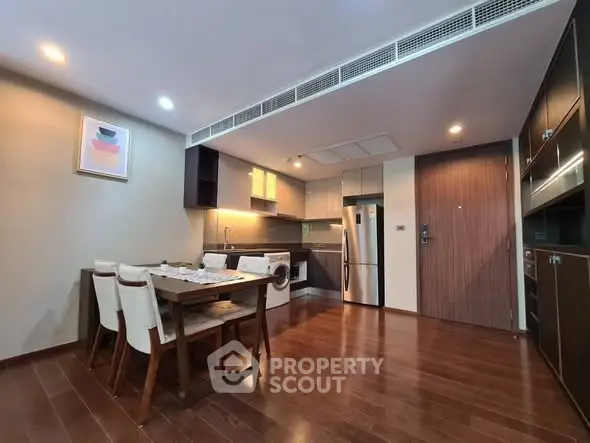Modern kitchen with wooden flooring and dining area in open layout apartment.