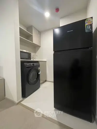 Modern compact kitchen with black fridge, washing machine, and microwave in sleek design.