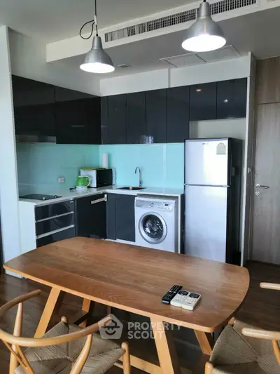 Modern kitchen with sleek cabinets, washing machine, and dining table in stylish apartment.