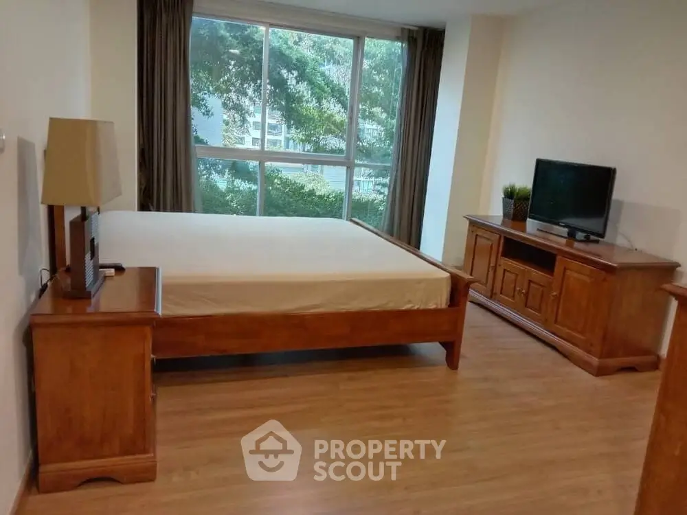 Spacious bedroom with large window and wooden furniture, offering a serene view.