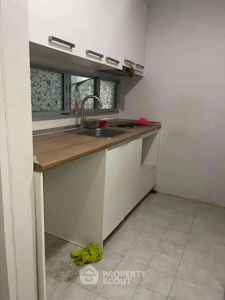 Compact kitchen with wooden countertop and white cabinets, featuring a single sink and tiled floor.