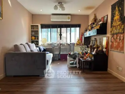 Cozy living room with wooden flooring and ample natural light, featuring a comfortable sofa and decorative elements.