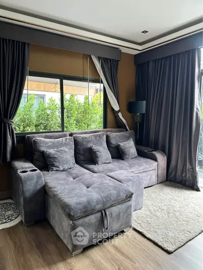 Luxurious living room with plush gray sofa, large windows, and elegant dark curtains.
