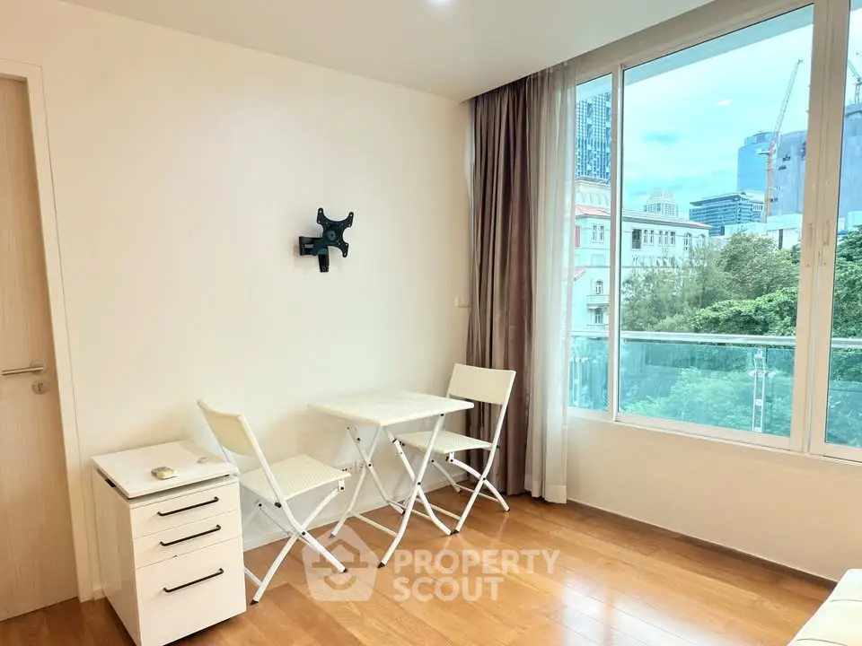 Bright and airy room with city view, featuring wooden floors and modern furniture.