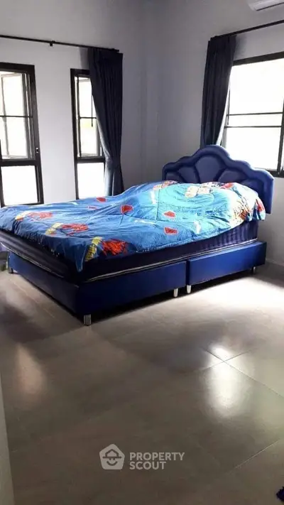 Spacious bedroom with modern blue bed and natural light from large windows.