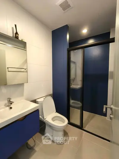 Modern bathroom with sleek blue and white design, featuring a glass shower and contemporary fixtures.