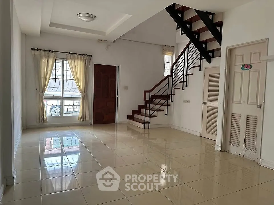Spacious living room with staircase and large window, perfect for family gatherings.