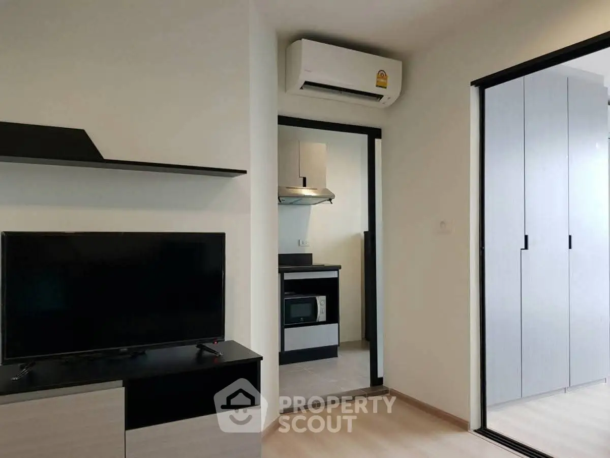Modern apartment interior with sleek TV setup and compact kitchen area.