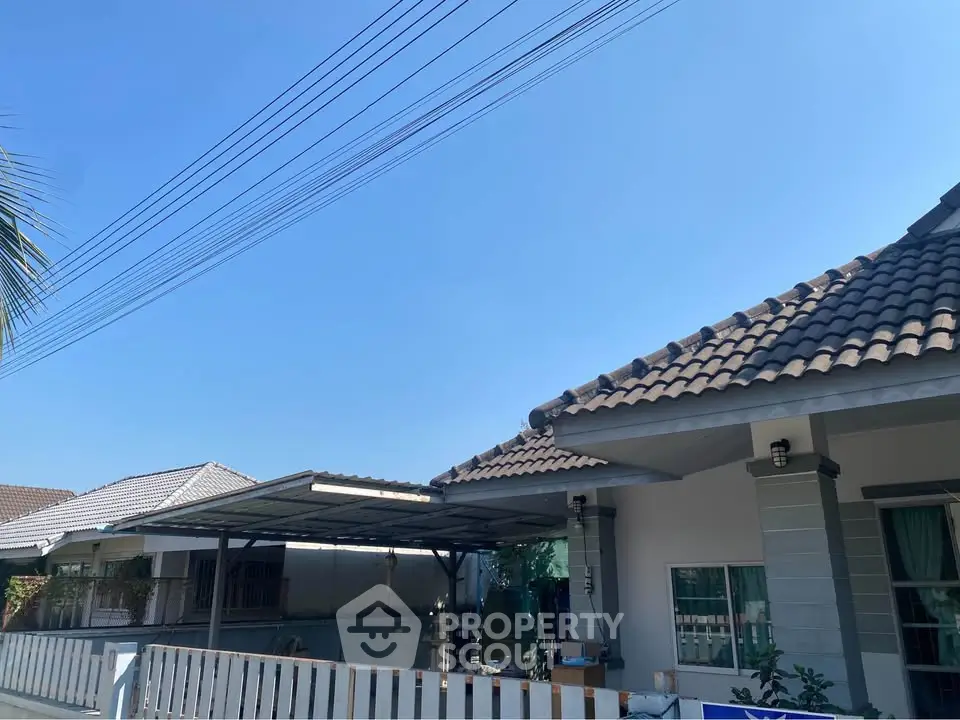 Charming suburban home with tiled roof and spacious carport under clear blue sky.