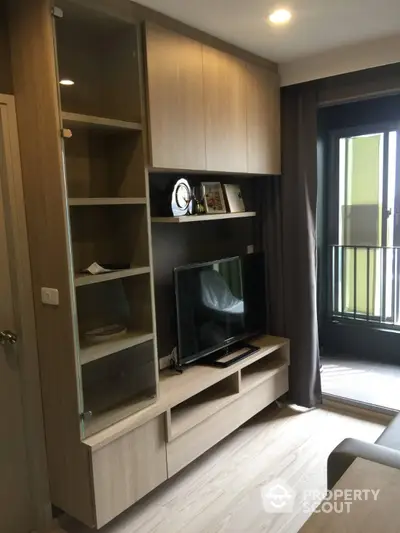 Modern living room with built-in wooden entertainment unit, sleek flooring, and access to a cozy balcony with natural light.