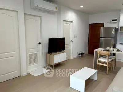 Modern living room with sleek furniture and open kitchen layout, featuring a flat-screen TV and air conditioning.