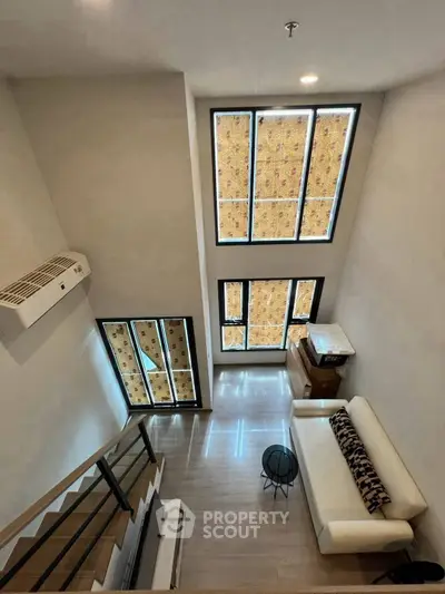 Modern loft-style living room with high ceilings and large windows, featuring a cozy sofa and sleek decor.