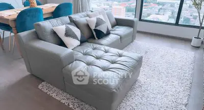 Modern living room with stylish gray sectional sofa and city view from large windows.
