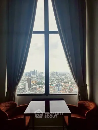 Stunning cityscape view from a high-rise apartment window with elegant curtains and cozy seating.