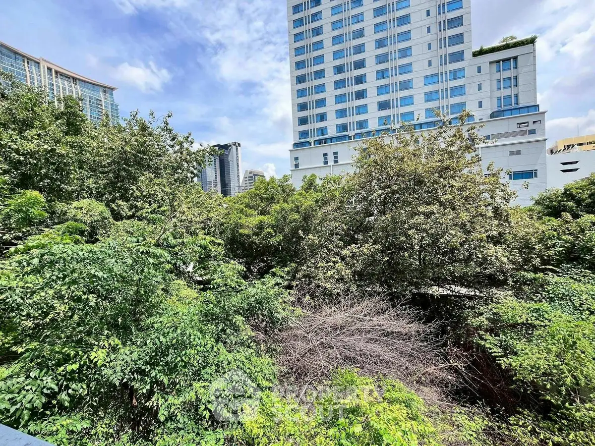 Urban view with lush greenery and modern high-rise buildings under a clear sky.