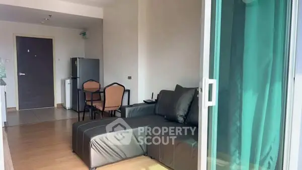 Modern living room with sleek furniture and natural light, featuring a compact dining area and kitchenette.