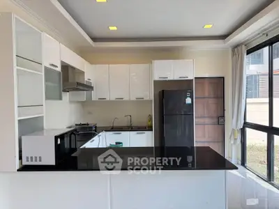 Modern kitchen with sleek white cabinets and black countertops, featuring a fridge and microwave.